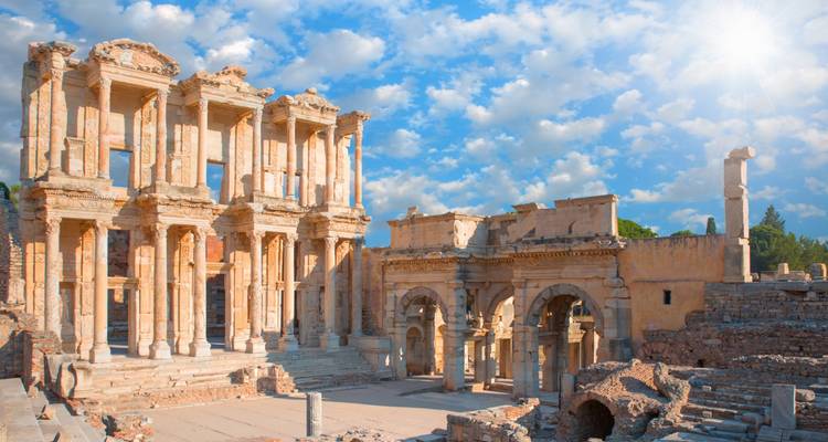 Ruines d'une ancienne bibliothèque avec une façade ornée sous un ciel lumineux.
