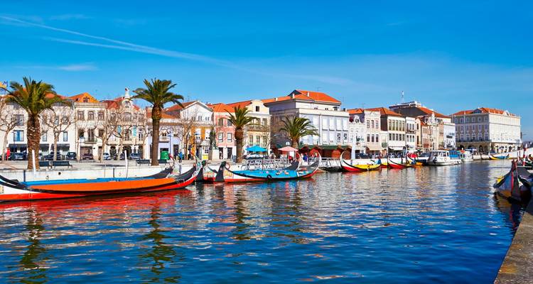 Canal à Aveiro avec des bateaux colorés de style gondole amarrés le long d'élégants bâtiments au bord de l'eau par une journée ensoleillée.