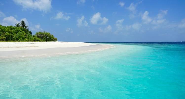Unberührter Strand mit weißem Sand und türkisfarbenem Wasser unter einem klaren blauen Himmel.