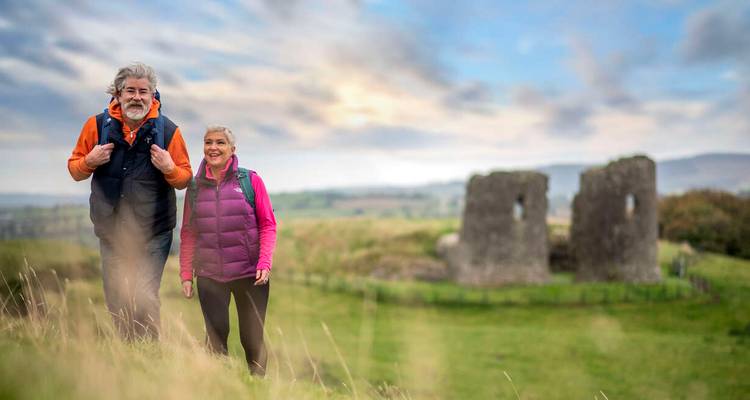 Un couple fait de la randonnée avec des ruines en arrière-plan.