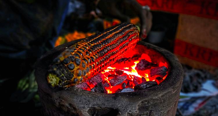 Maïs grillé sur un fourneau avec des braises incandescentes.