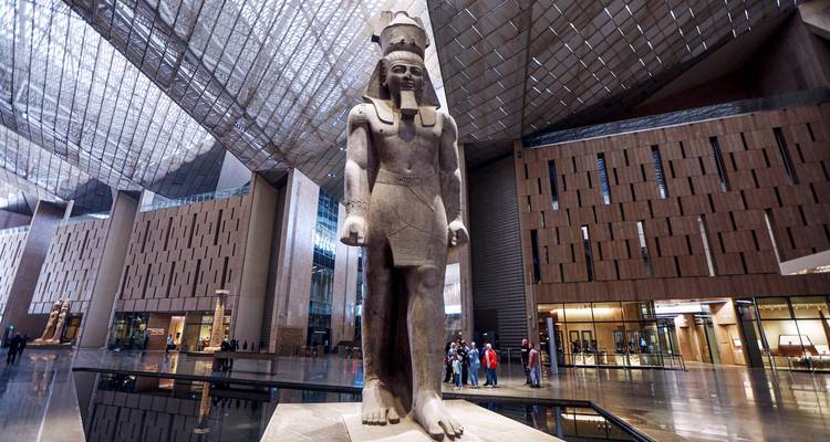 Grande statue égyptienne dans un cadre de musée moderne avec des personnes qui observent.