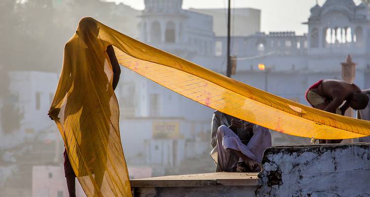 Persoon die kleurrijke stof buiten droogt met traditionele architectuur.