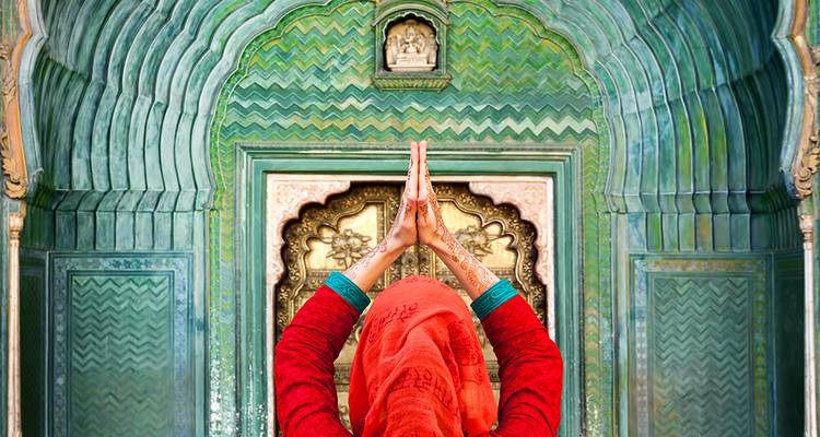 Persoon in traditionele kledij biddend bij sierlijk versierde deuropening.