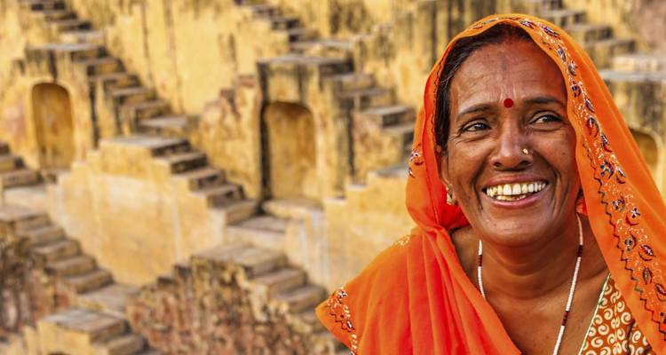 Glimlachende vrouw in kleurrijke sari bij een trappenput.
