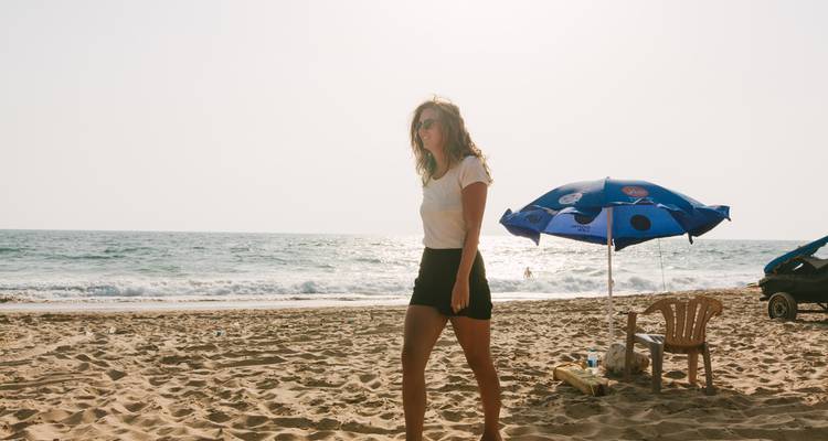 Persoon die op een strand loopt met een parasol op de achtergrond.