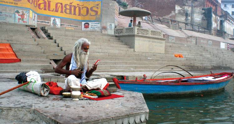 Heilige man zittend bij trappen aan een rivier met een boot in de buurt.