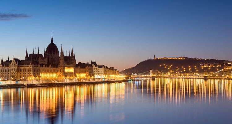 Le Parlement illuminé de Budapest brille au bord du Danube à l'heure bleue, se reflétant dans l'eau.