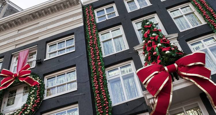 Une façade de maison de canal noire et haute à Amsterdam est somptueusement ornée de gigantesques nœuds rouges, de guirlandes et de boules pour Noël.