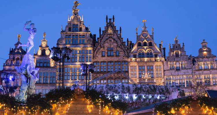 Las casas gremiales ornamentadas de la Grote Markt de Amberes brillan con luces festivas a la hora azul sobre los puestos tipo chalé.