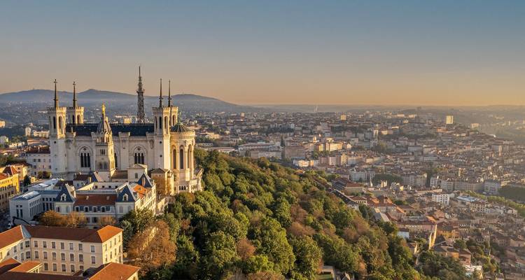 Panorama aéreo de Lyon con la Basílica de Notre-Dame de Fourvière en la cima de la colina brillando con luz dorada sobre el horizonte de la ciudad.