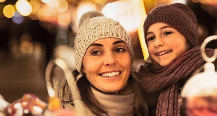 Mère et enfant souriants dans un cadre festif avec des lumières.