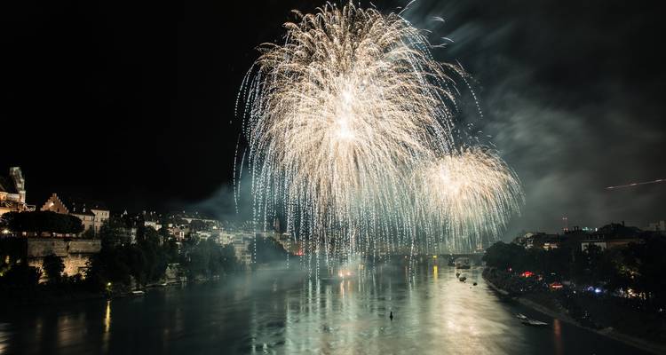 Des feux d'artifice blancs spectaculaires cascadant au-dessus d'une rivière la nuit avec des bâtiments de la ville bordant le front de mer.