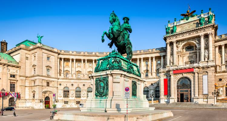 Statue équestre sur la Heldenplatz avec les grandes arches du palais de la Hofburg de Vienne illuminées par la lumière matinale.