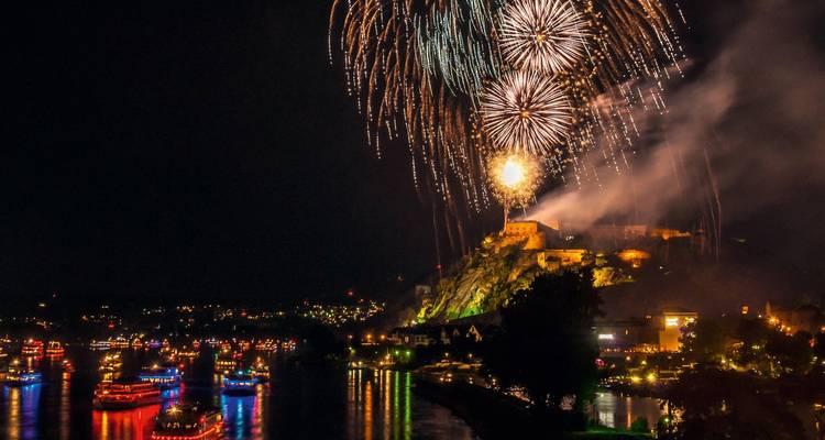 Fireworks over a river with boats and a fortified structure.