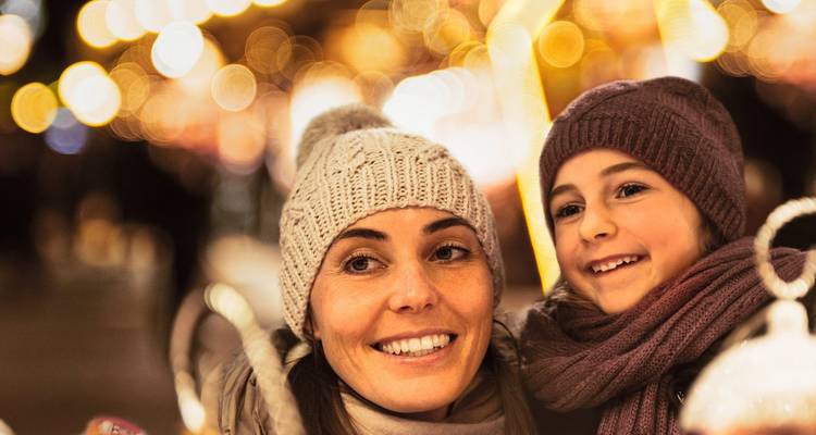 Mère et enfant à un marché de Noël festif avec des lumières colorées en arrière-plan.