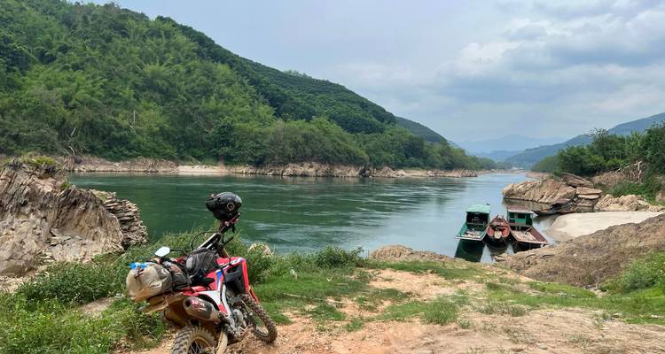 Moto et bateaux sur une berge avec des collines.