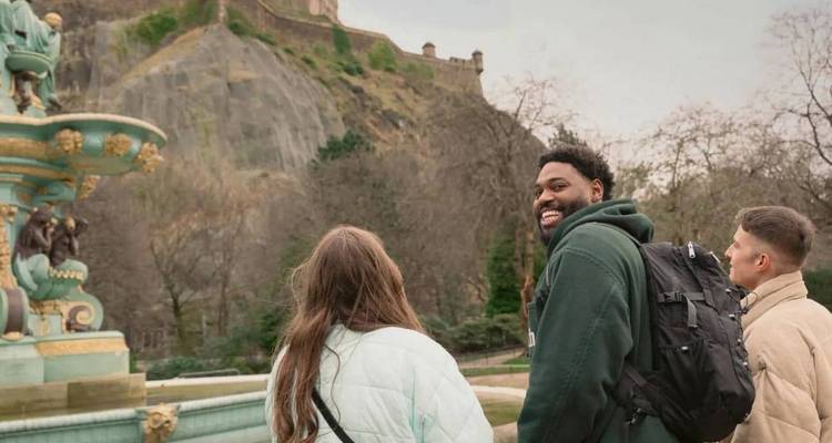 Los viajeros admiran el Castillo de Edimburgo desde una fuente en un parque en un día nublado