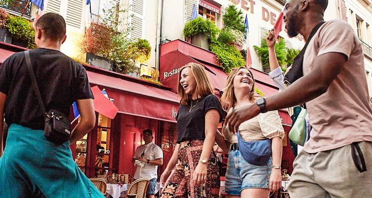 Grupo animado paseando junto a las coloridas terrazas de cafés parisinos riendo y disfrutando de la tarde.