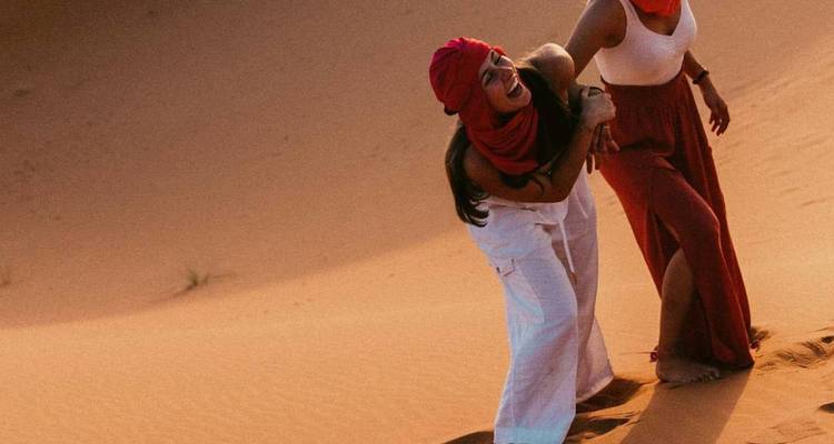 Deux femmes vêtues de foulards riant en gravissant des dunes de sable sous le soleil