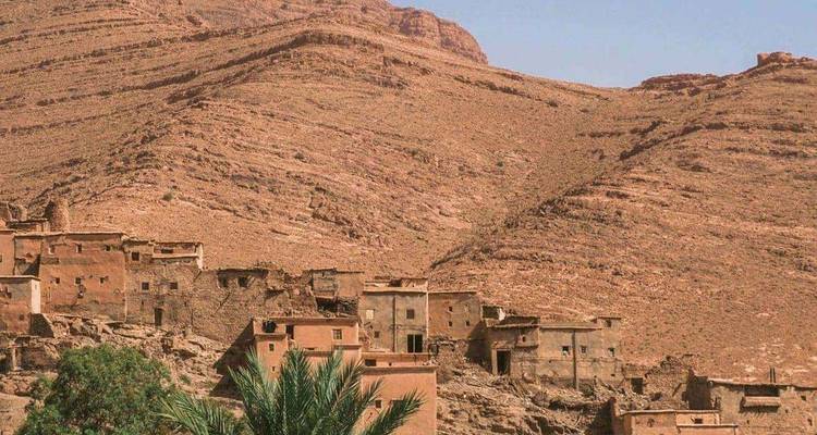 Village de versants en terre avec des maisons en adobe aux toits plats, situé face à des montagnes rocheuses arides