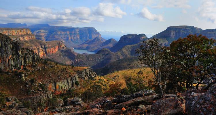 Vista panorámica amplia sobre profundas paredes verdes del cañón y río serpenteante bajo un cielo azul brillante con nubes dispersas.