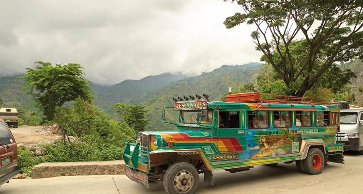 Jeepney sur la route avec un arrière-plan montagneux.