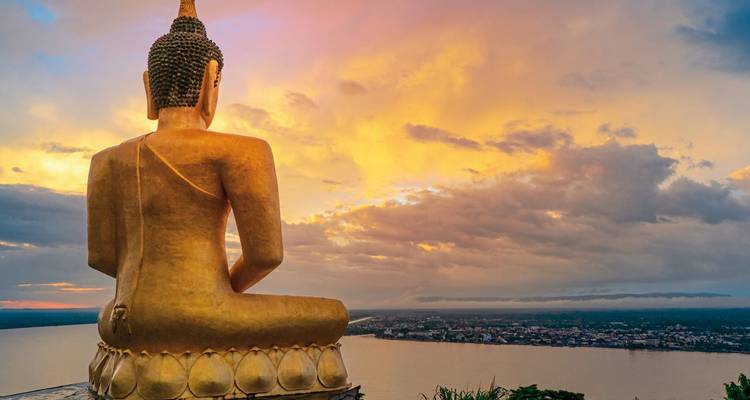 Large golden Buddha statue overlooking a city at sunset