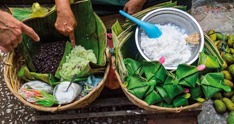 Hands pointing to street food wrapped in banana leaves