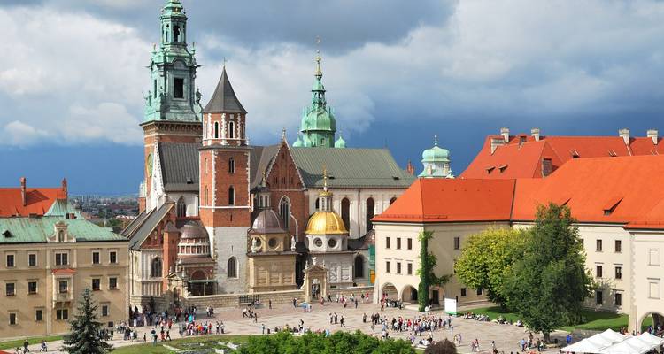 Vista amplia de la Catedral de Wawel y el complejo del castillo con multitudes en un gran patio bajo nubes dramáticas.
