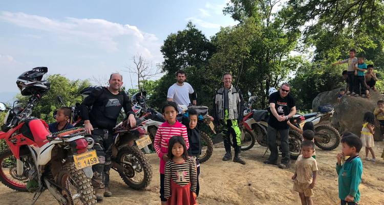 Groep motorrijders en lokale kinderen in een landelijke omgeving.