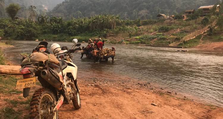 Crossmotor op een rivieroever met een groep mensen op een vlot.