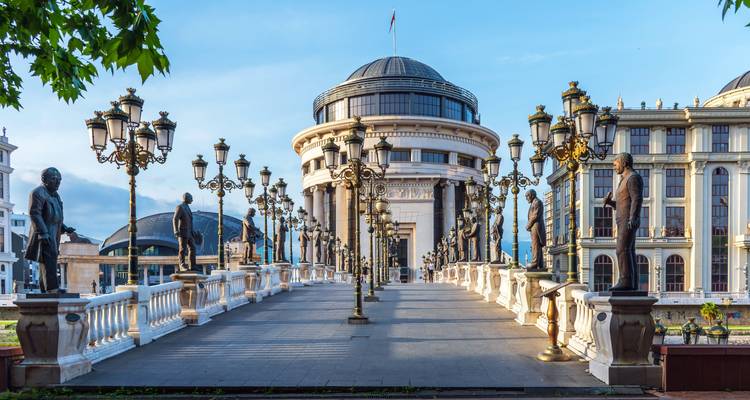 Bridge lined with statues leading to a domed building.