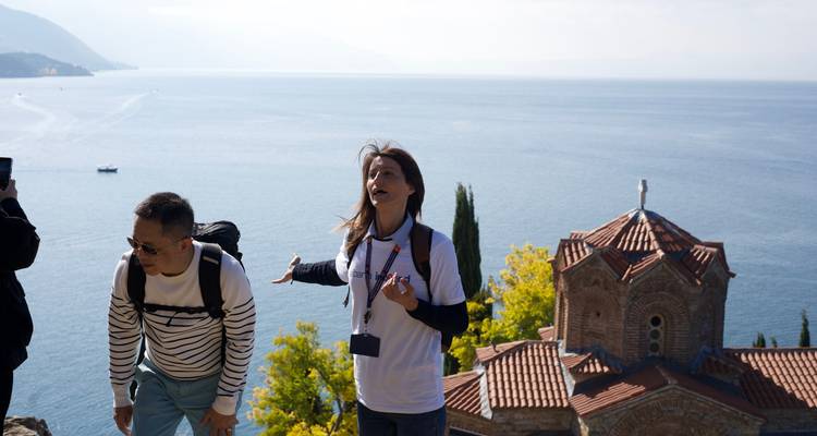 Tour guide explaining to tourists on a hill by the sea.