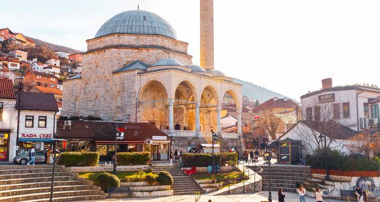 Historic mosque in a bustling square with mountains in the background.