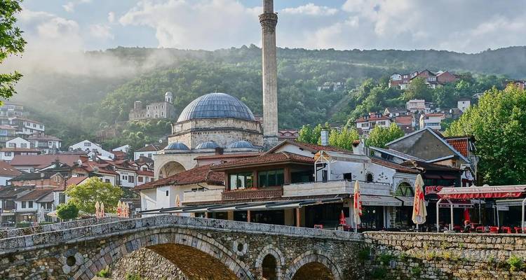 Historic town with a mosque, bridge, and mountain backdrop.