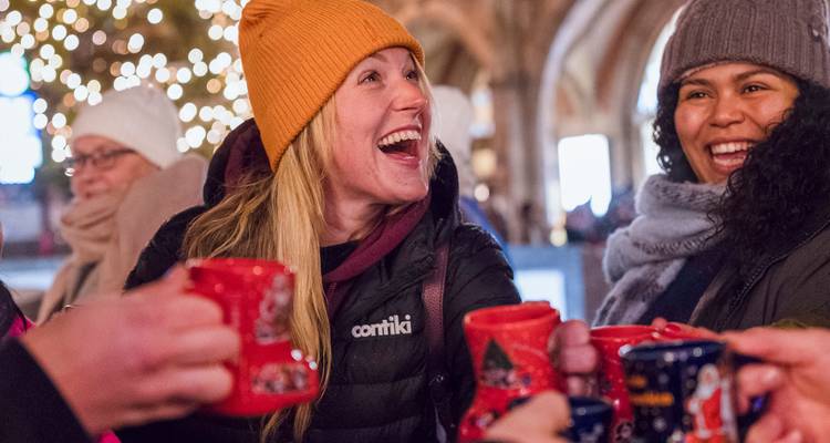 Amigos brindan con tazas coloridas de recuerdo bajo luces festivas en un mercado navideño europeo.