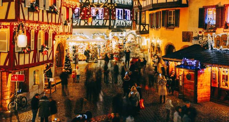 Festive Christmas market in half-timbered Alsace town illuminated by twinkling lights and bustling crowds