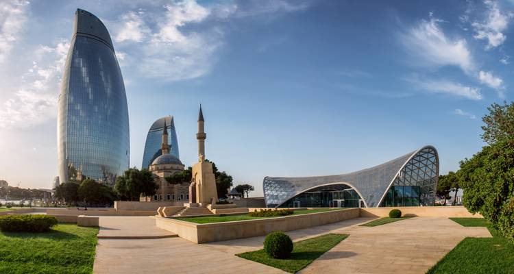 Architecture moderne aux courbes élégantes, une mosquée et les emblématiques tours Flamme créent un horizon saisissant à Bakou sous un ciel dégagé.