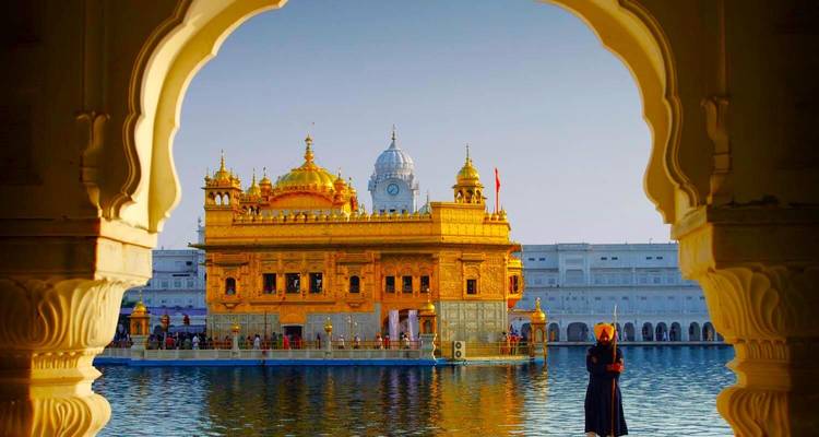 Temple doré vu à travers une arche, personne debout au bord de l'eau.