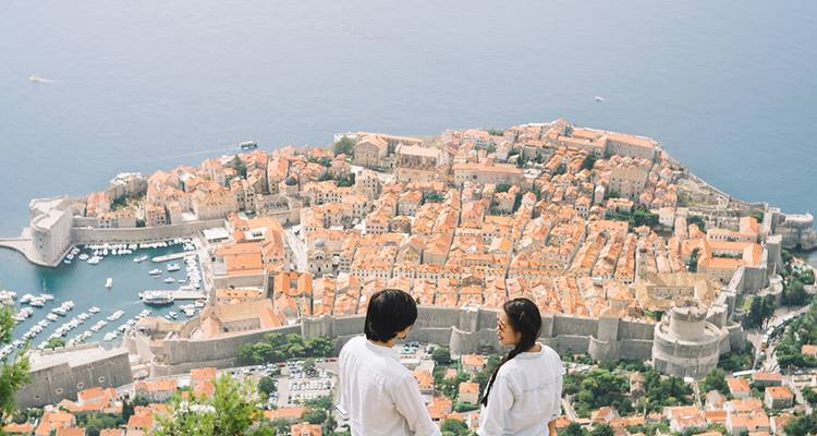 Overlooking Dubrovnik’s walled old town and marina from a high viewpoint with a young couple admiring the panoramic scene