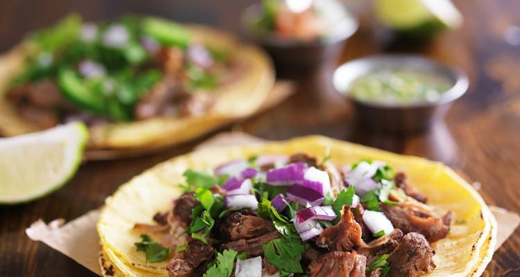 A close-up of tacos with meat and vegetables on a table.