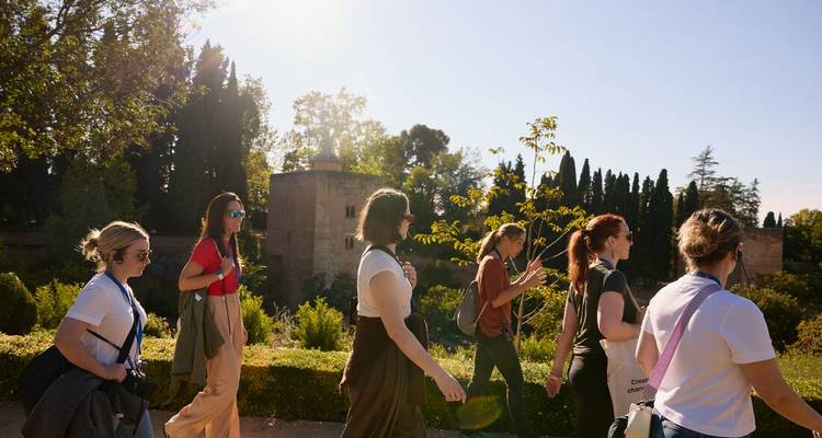 Un groupe de voyageurs marche dans des jardins ensoleillés le long d'anciens murs de pierre à Grenade.