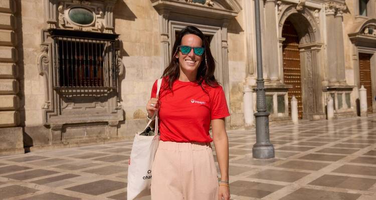 Femme souriante avec des lunettes de soleil se tient sur une place pavée devant la cathédrale de Grenade.