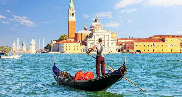 Un gondolier en chemise rayée pousse une gondole vers la basilique San Giorgio Maggiore à dôme blanc qui se dresse de l'autre côté de la lagune bleue de Venise.