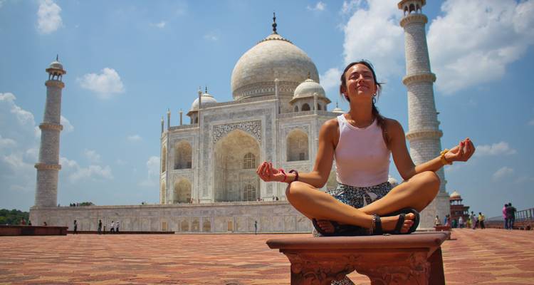 Frau meditiert vor dem Taj Mahal unter einem klaren blauen Himmel.