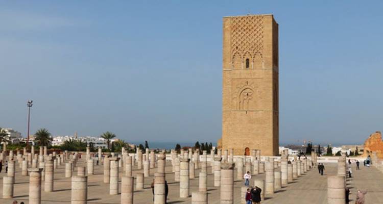 Ein hoher Minarett mit Ruinen und ein Platz mit gehenden Menschen.