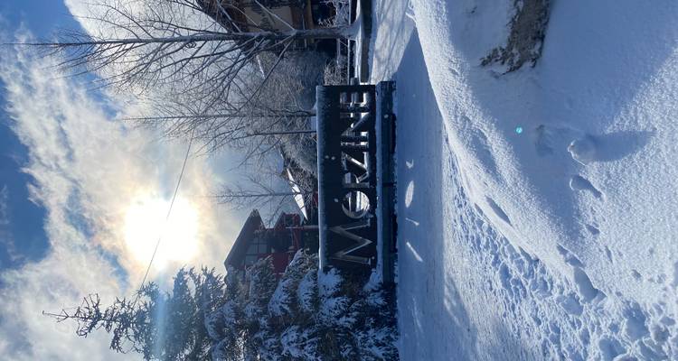 Scène de rue enneigée avec un grand panneau métallique « Morzine » sous un soleil d'hiver éclatant.