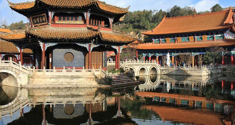Pabellón tradicional chino a orilla del lago con techo ornamentado reflejado perfectamente en aguas tranquilas.
