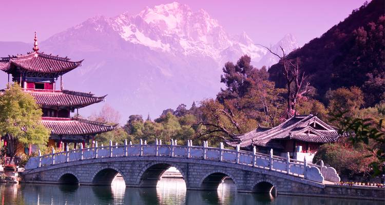 Puente de piedra y pagoda frente a picos nevados dramáticos, bañados en tonos de crepúsculo magenta.
